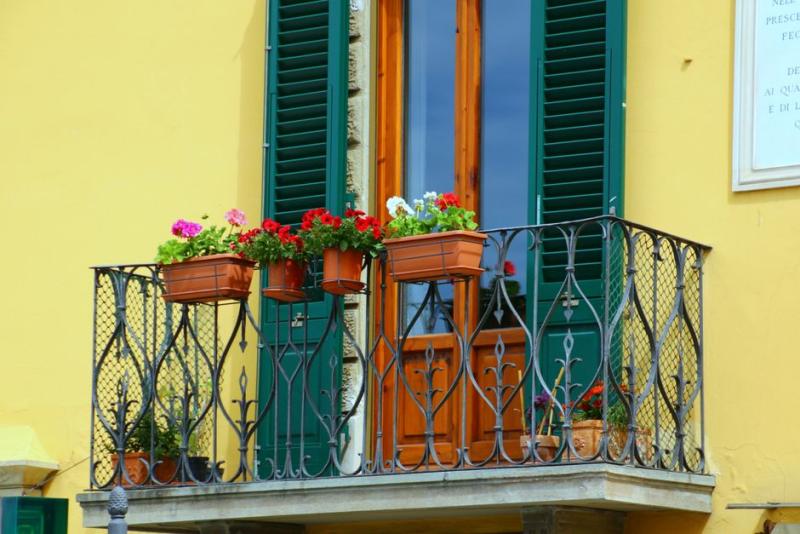 Balcon plein sud avec des jardinières de géraniums colorés accrochées à la rambarde en fer forgé